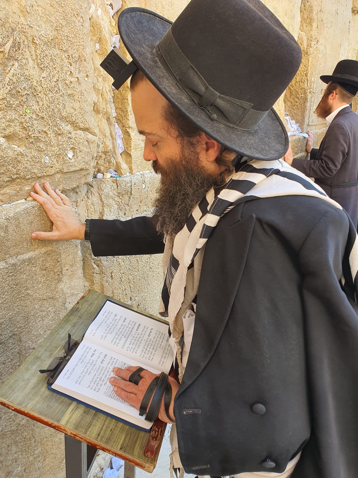 Rav Reuven Weinreb praying at the Western Wall, his hand resting on the stone.